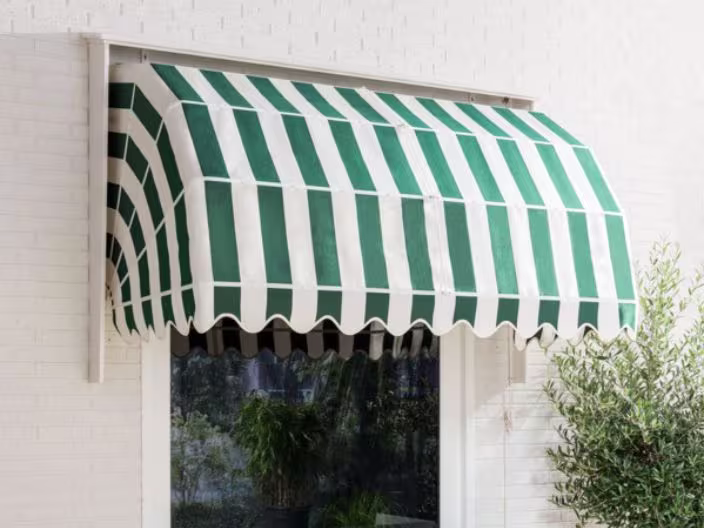 Groen-wit gestreepte zonnescherm boven een raam op een witte bakstenen muur, met een plant zichtbaar aan de rechterkant.