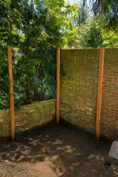 Hoek van een tuin met een bakstenen muur begroeid met mos, houten palen en groene bomen op de achtergrond.