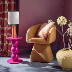 Theo-Bert Pot collectie in een moderne woonkamer: een goudbruine fauteuil, roze bijzettafel met lamp en een vaas met witte bloemen tegen paarse muur.