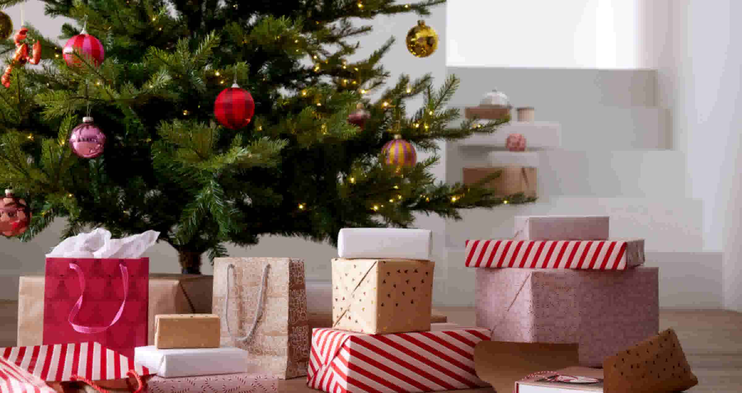 Versierde kerstboom met kleurrijke ballen en lichtjes, omringd door feestelijk ingepakte cadeaus in rood, wit en goud.