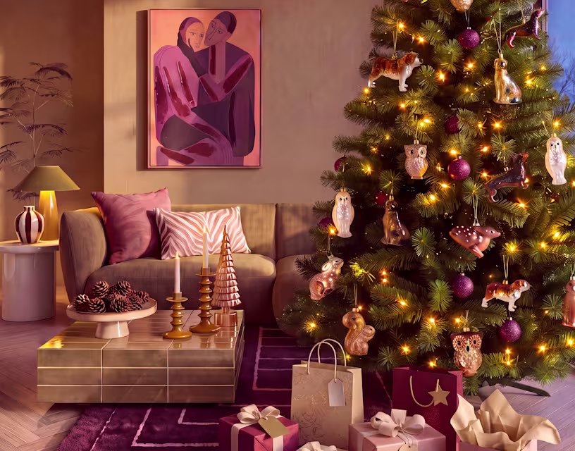 Gezellige woonkamer met verlichte kerstboom versierd met dierenornamenten, beige bank en roze-paarse woondecoratie.