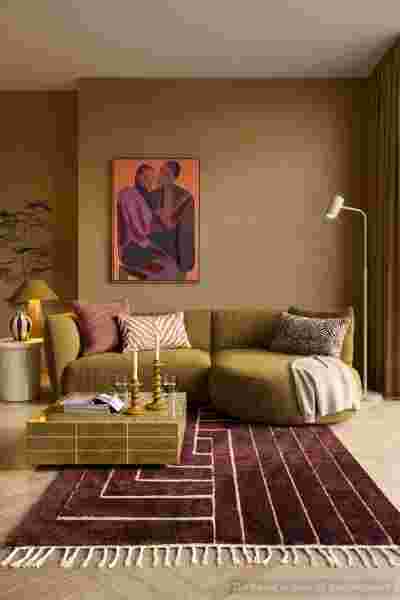 Moderne woonkamer met olijfgroene bank, bordeauxrood tapijt en abstract kunstwerk aan beige muur