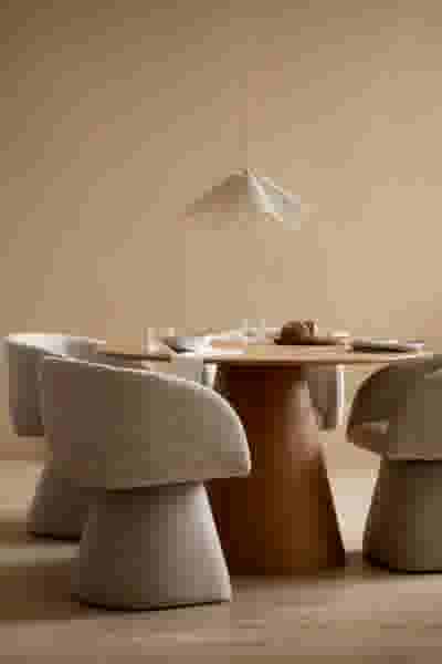 Moderne eetkamer met ronde houten tafel, beige stoelen en een delicate hanglamp boven een gedekte tafel.