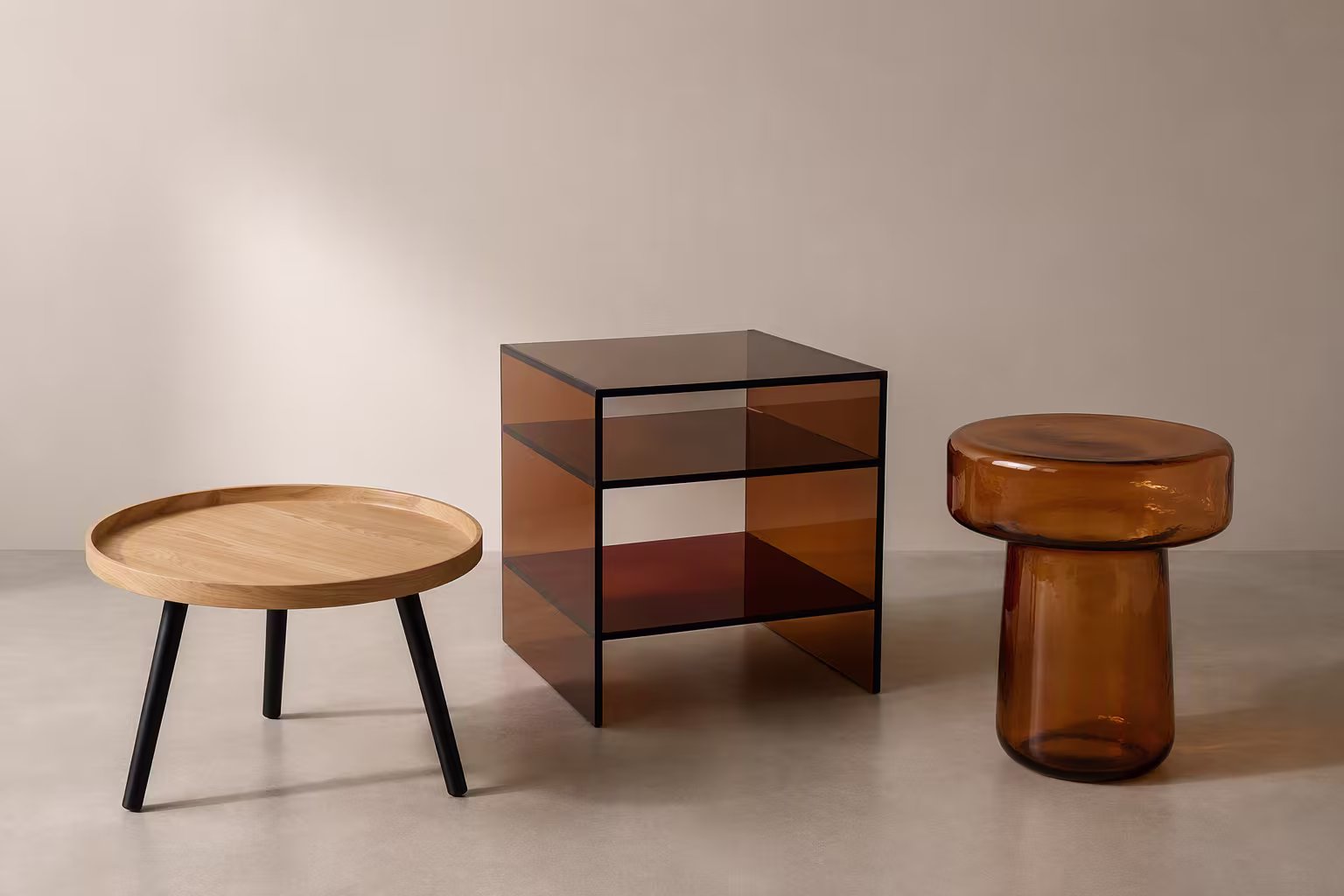 Drie designmeubels: een houten ronde tafel met zwarte poten, een amber glazen kubustafel en een amberkleurige glazen paddenstoelkruk.
