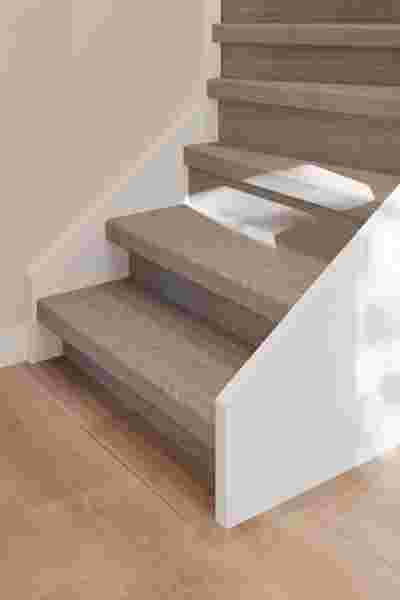 Houten trap met grijsbruine treden en witte stootborden in een lichte ruimte met beige muren en lichthouten vloer.