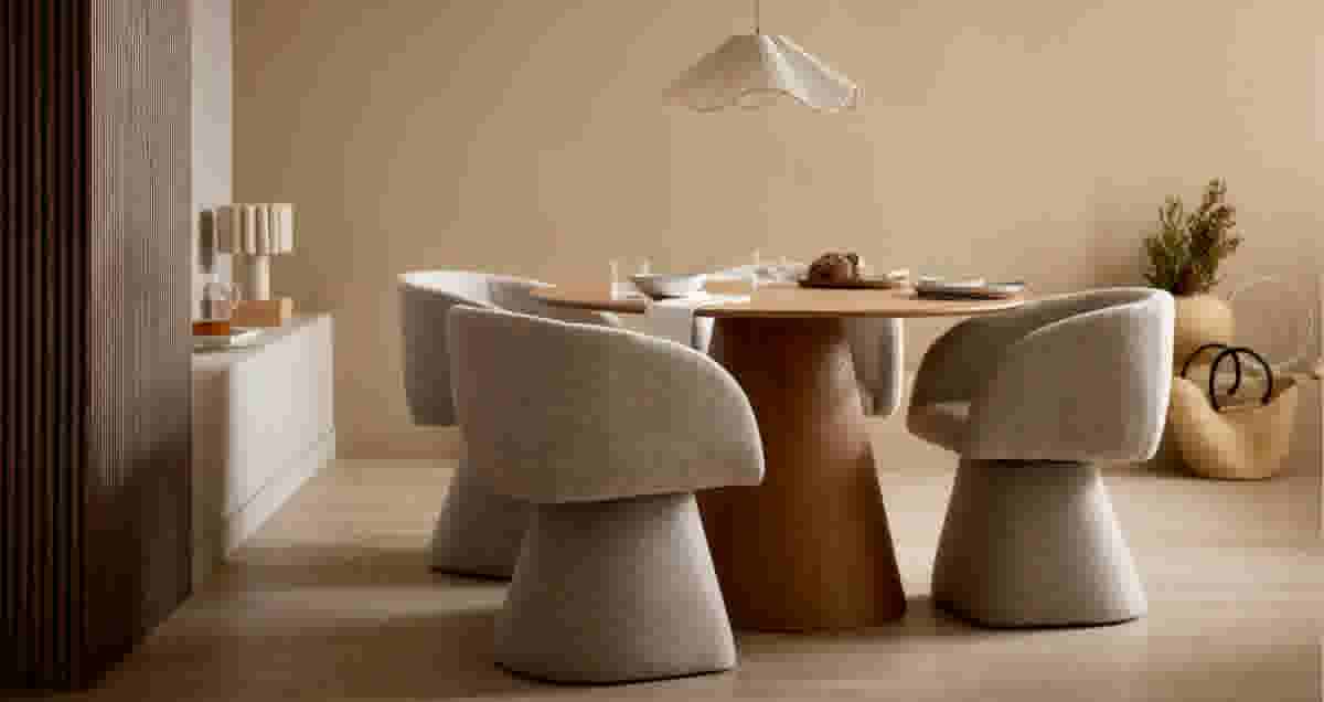 Minimalistische eetkamer met beige stoelen aan een houten tafel, hanglamp en dressoir in warme, neutrale tinten.
