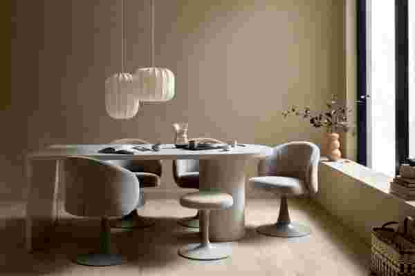 Moderne eetkamer met ronde tafel, grijze stoelen, witte hanglampen en een vaas met takjes in een warme beige ruimte.