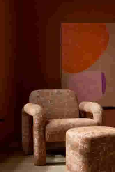 Bruine fauteuil met bijpassende poef tegen terracotta muur met abstracte kunst met oranje en paarse vormen.