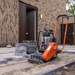 Oranje gehuurde trilplaat van Rent Partner Boels naast stapel grijze stenen voor een nieuwbouwhuis