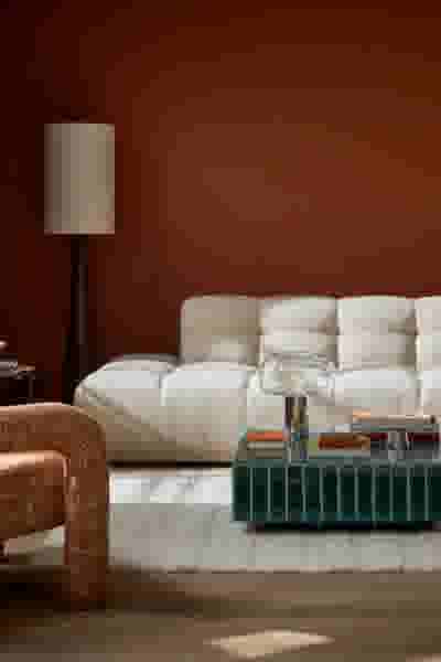 Modern woonkamer met roestbruine muren, crèmekleurige bank, groene glazen salontafel en staande lamp met beige kap.