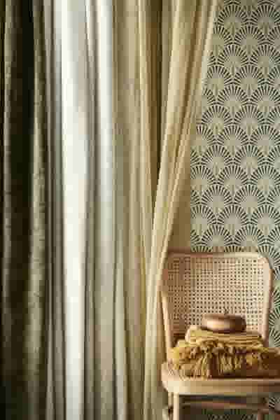 Elegante interieur met rieten stoel, groene en beige gordijnen, decoratief behang met waaierpatroon en gouden accessoires.