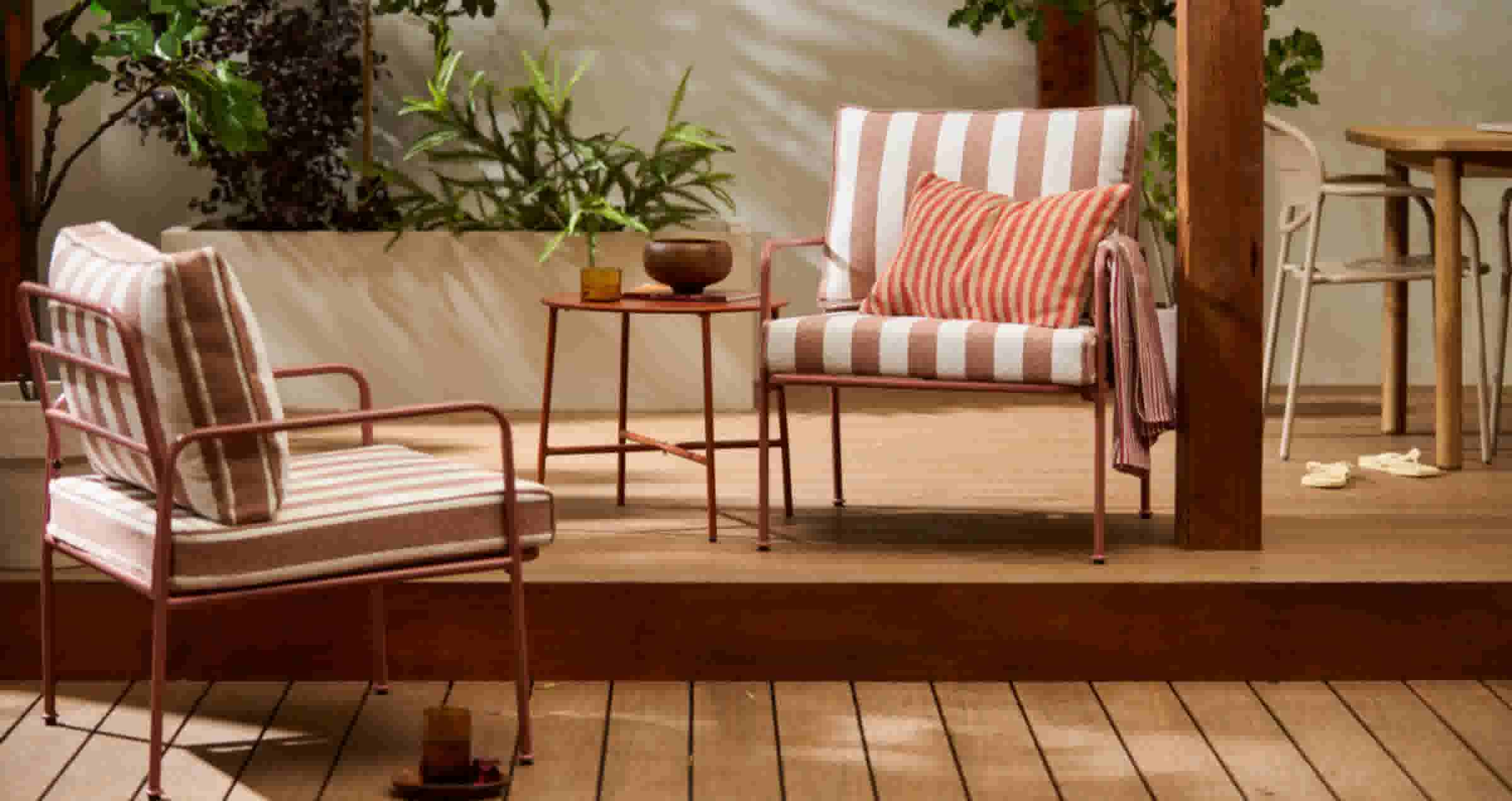 Gezellige terrashoek met roze gestreepte stoelen, een bijzettafel en groene planten in een lichte, warme ruimte.