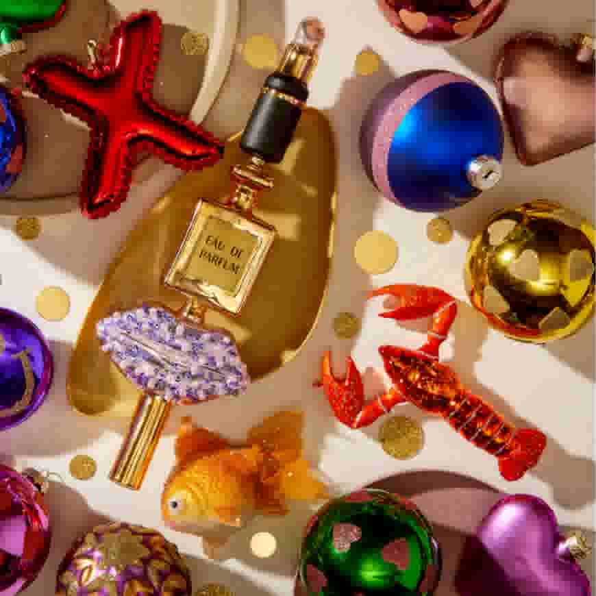 Kleurrijke kerstornamenten met een parfumflesje, zeester, kreeft, vis en hartvormige decoraties op een lichte achtergrond.