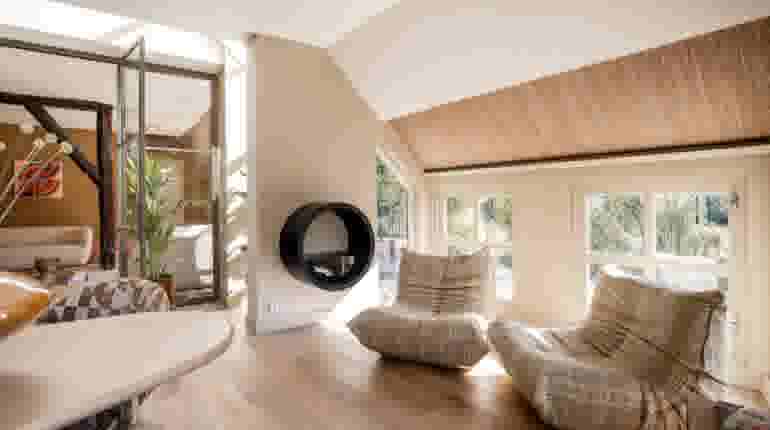 Lichte woonkamer met rieten plafond, grote ramen, beige loungestoelen en ronde zwarte wandspiegel in moderne stijl.
