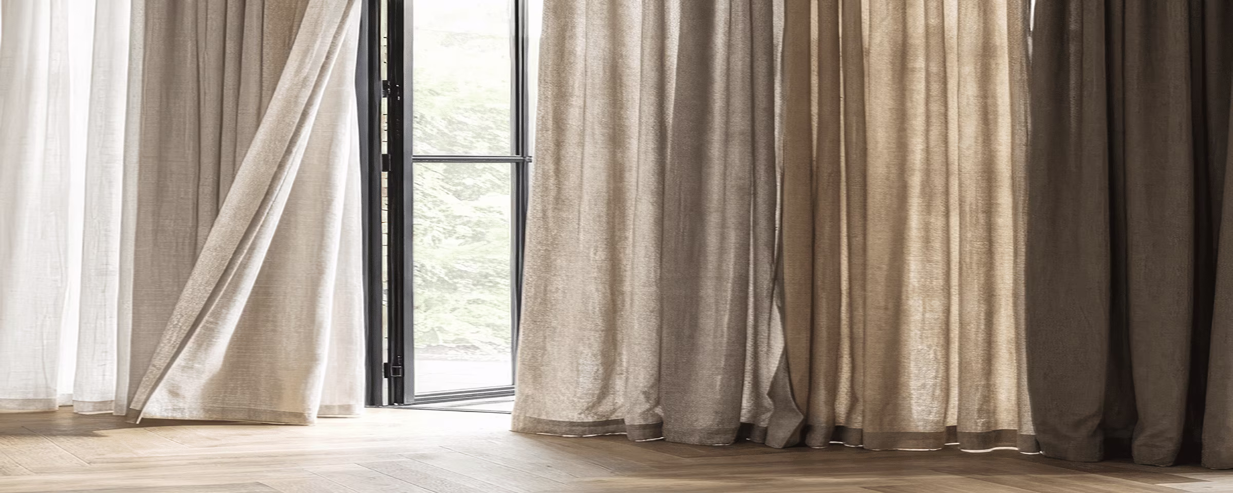 Beige en witte linnen gordijnen hangen voor een open glazen deur met uitzicht op groen, op een lichte houten vloer.