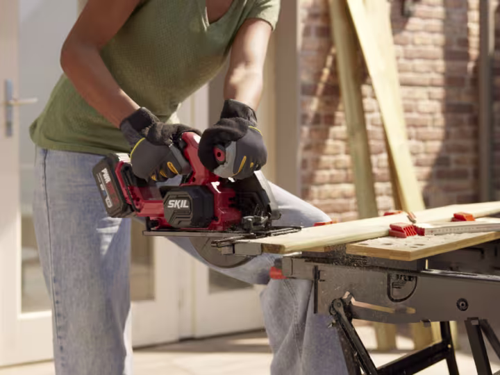 Persoon zaagt een houten plank op maat met een accu-cirkelzaag op een werkbank