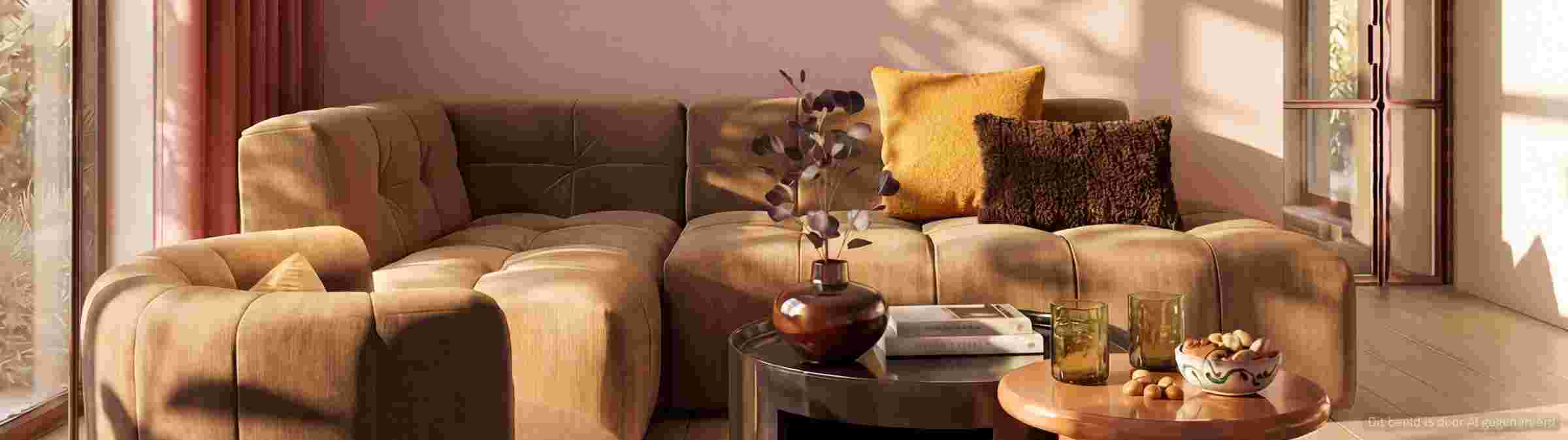 Moderne beige gestoffeerde bank met gele en bruine kussens in een zonnige woonkamer met roze muren en ronde salontafel.