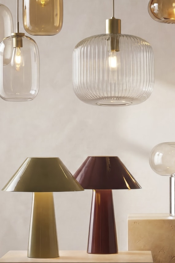 Moderne hanglampen met glazen kappen en tafellamp in goud en bordeauxrood tegen een witte achtergrond.