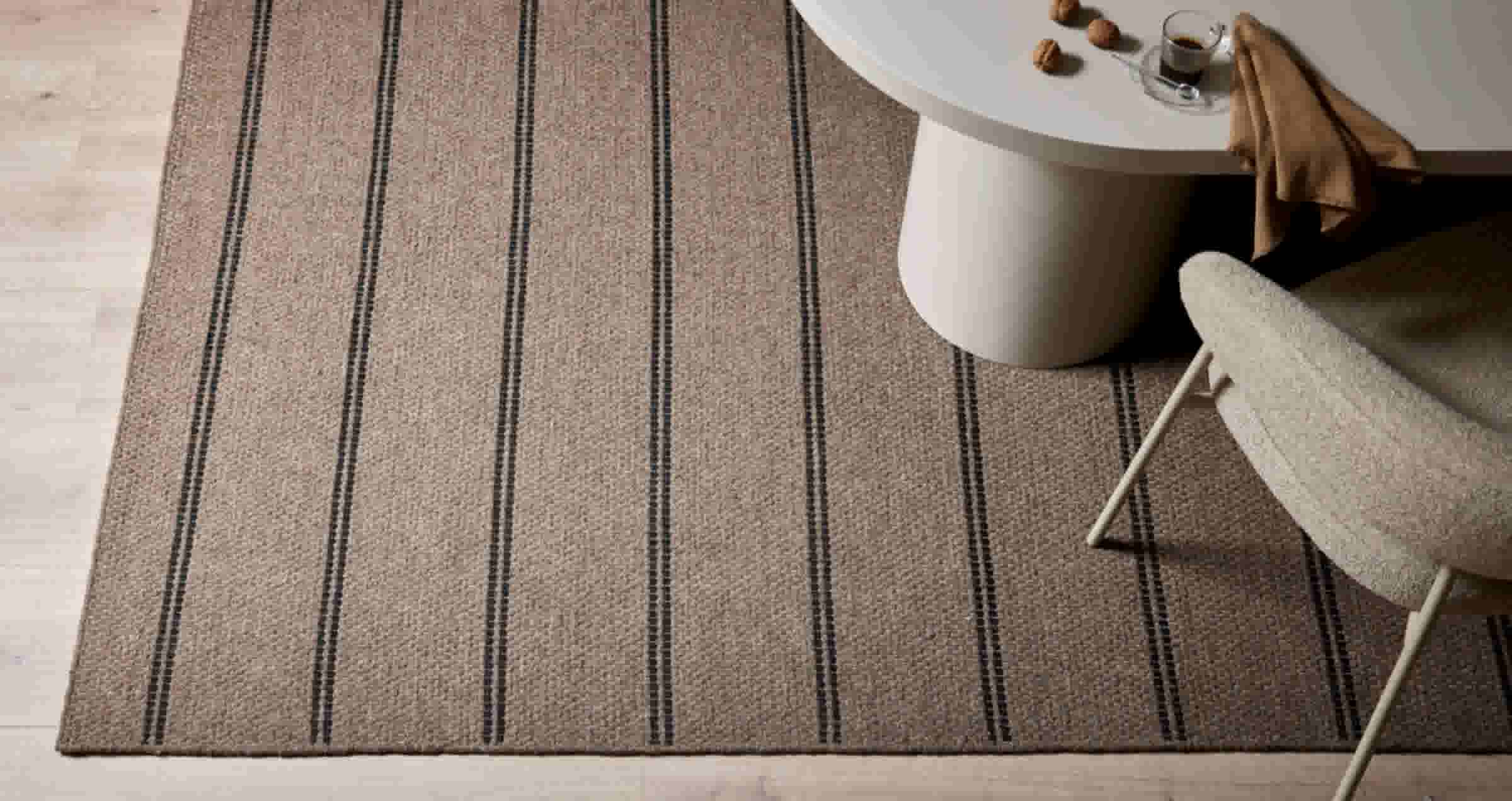 Beige tapijt met zwarte strepen, witte salontafel met noten en espresso, en een deel van een lichte fauteuil zichtbaar.