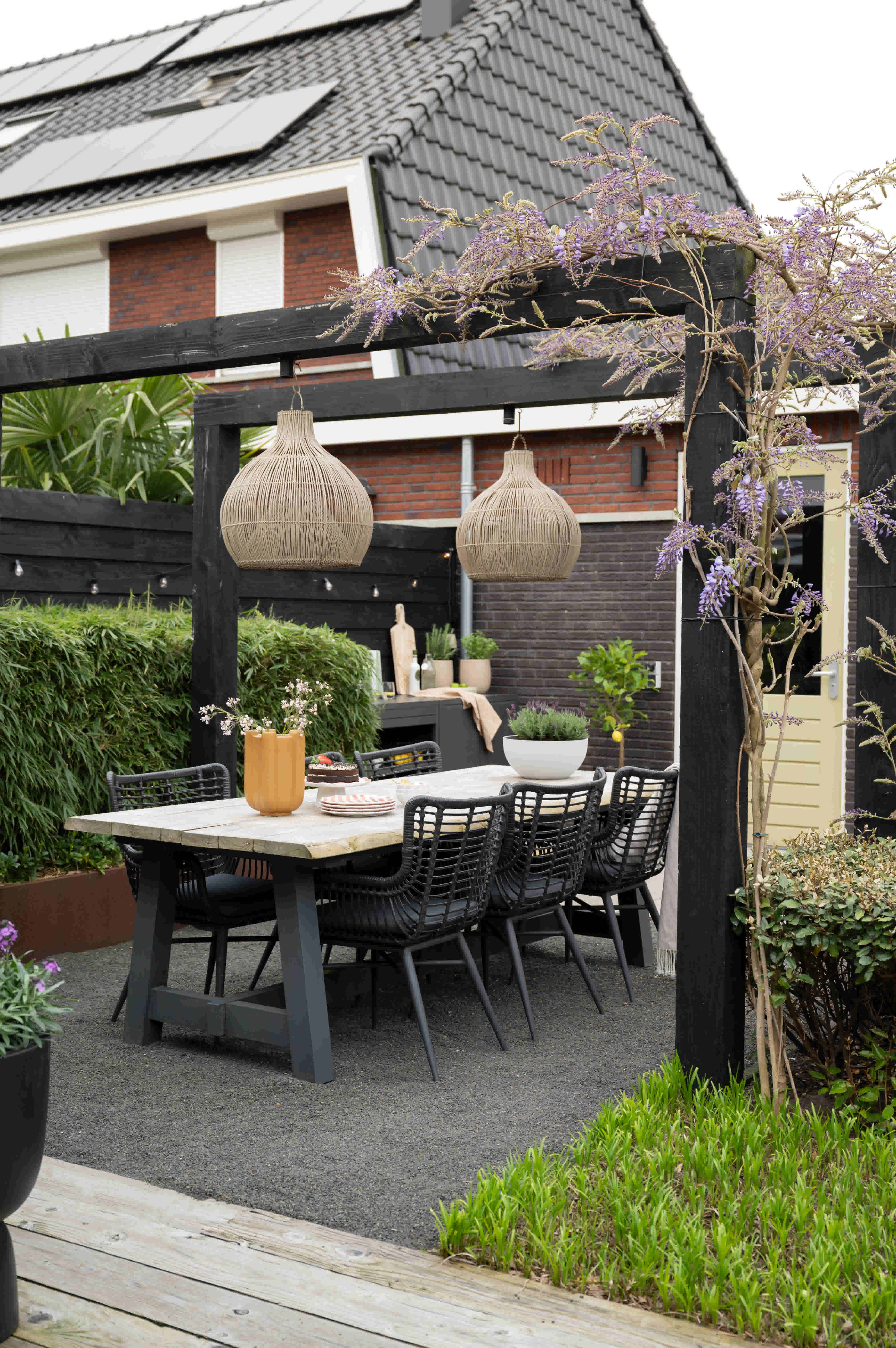 Tuineettafel onder pergola met zwarte tuinstoelen