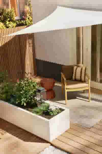 Zonnig terras met houten vloer, witte plantenbak met groen, gele stoel met kussen en wit zonnezeil.
