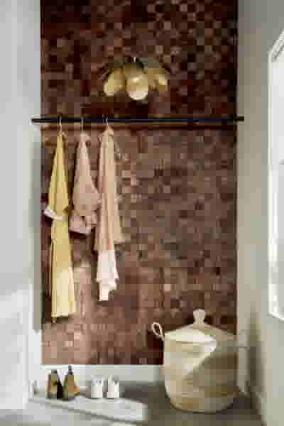 Badkamer met houten wand, zwarte kapstok met handdoeken, bloem-vormige lamp en gevlochten mand.