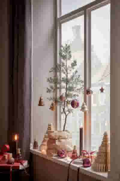 Sfeervol kerstvensterbank met kleine boom, houten decoraties en hangende ornamenten, met uitzicht op daken buiten.