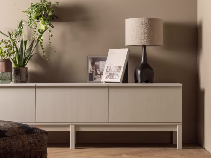 Modern tv-meubel met zwarte lamp, tijdschrift en groene planten tegen beige muur in stijlvol interieur.