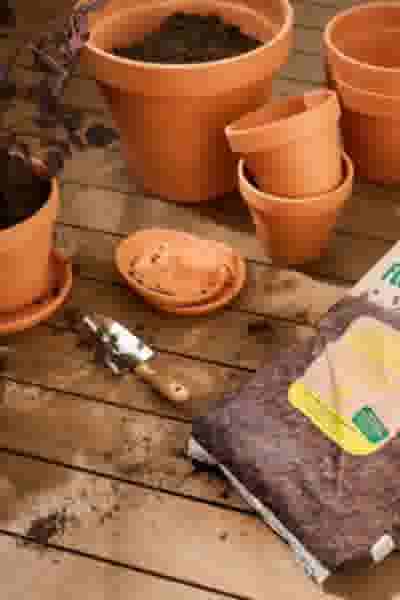 Terracotta bloempotten, een schepje en een zak potgrond op een houten tafel, klaar voor het verpotten van planten.