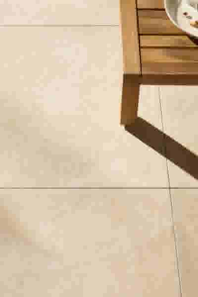 Beige tegelvloer met een houten tafel in de hoek en een wit bord. Schaduw van de tafel valt op de vloer.