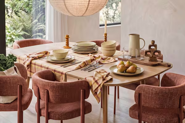 Eetkamer met gedekte houten tafel, terracotta kleurige stoelen, beige servies, servetten en kaarsenstandaards