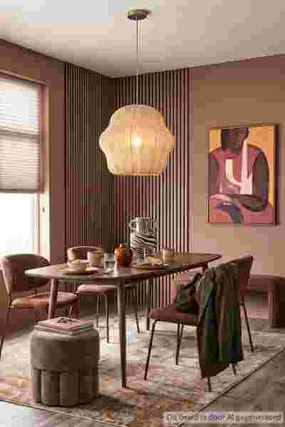 Moderne eetkamer met bruine tinten, ovale houten tafel, fluwelen stoelen, geometrische hanglamp en abstract kunstwerk.