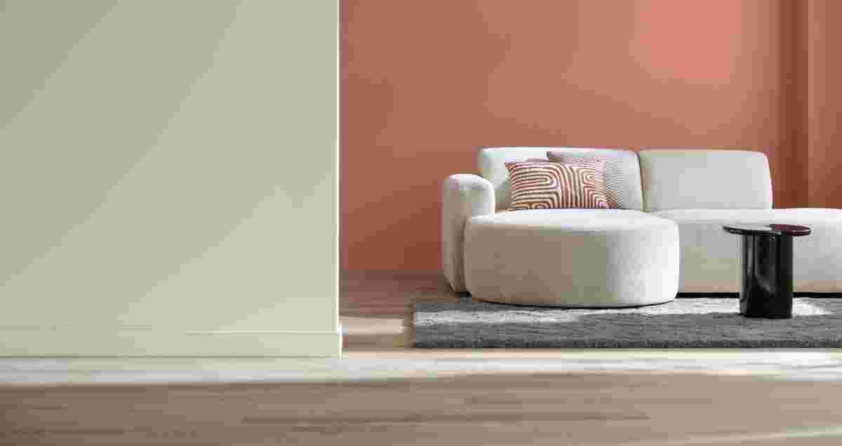 Moderne woonkamer met crèmekleurige bank, gestreept kussen en roze muur op houten vloer in contrast met witte muur.