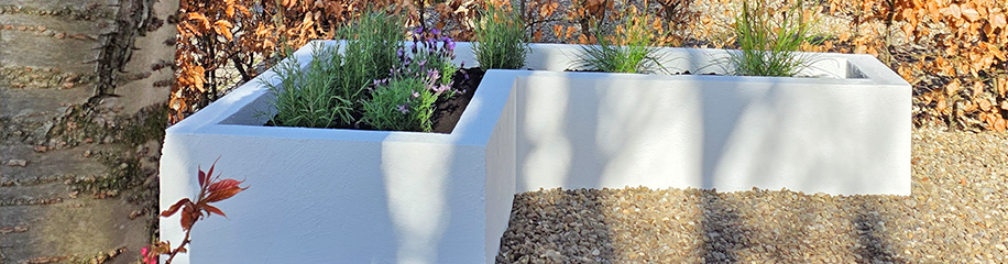Witte verhoogde plantenbakken met planten in L-vorm geplaatst op een grindpad.