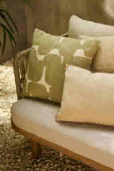 Gezellige zithoek in de tuin met beige bank, groene en crèmekleurige sierkussens met grint en planten