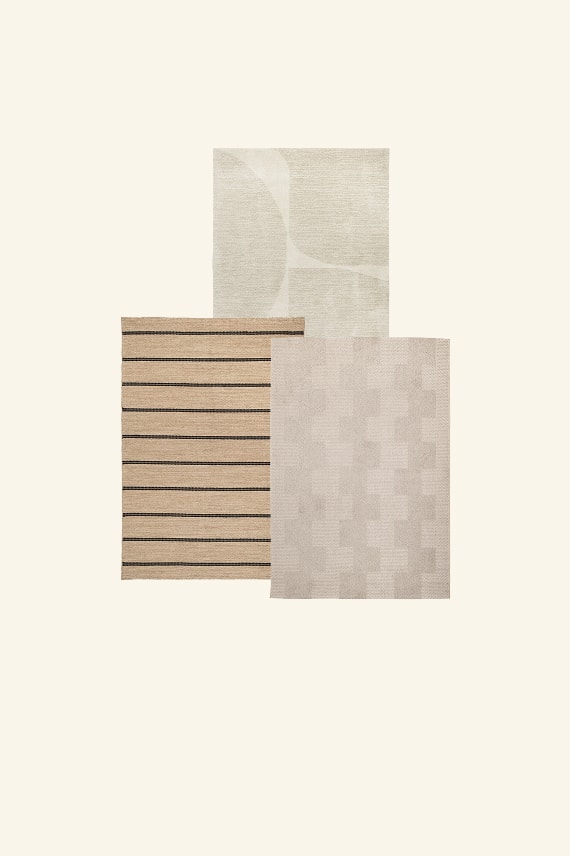 Drie overlappende tapijten in neutrale tinten: beige met zwarte strepen, lichtgrijs en crèmewit.