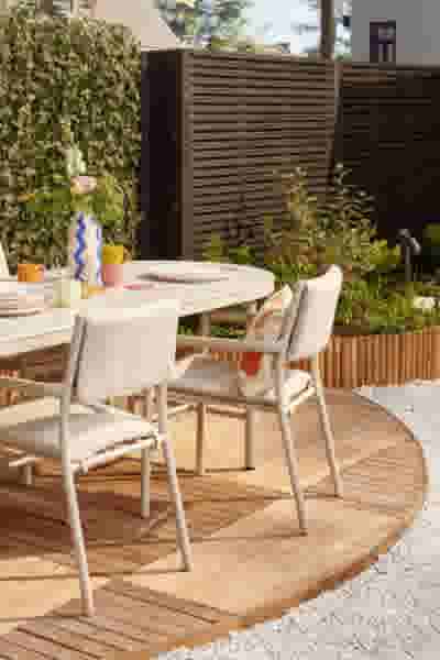 Beige tuinset met ovale tafel en stoelen op houten terras, versierd met kleurrijke vazen en borden, omgeven door groen.