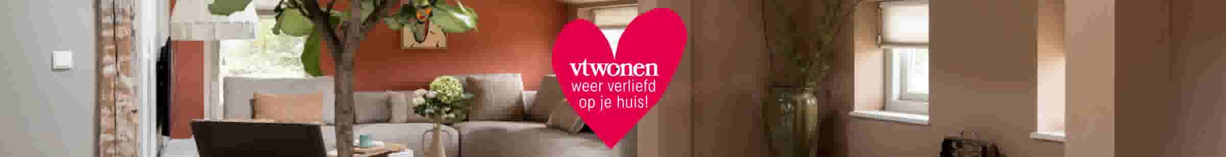 Modern woonkamerinterieur met roze hart en tekst 'vtwonen weer verliefd op je huis!' in het midden.