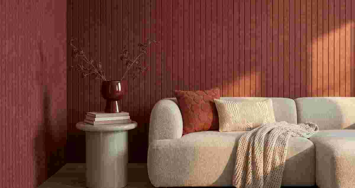 Beige bank met kussens en plaid voor een rode ribbelwand. Bijzettafel met boeken en rode vaas met droogbloemen.
