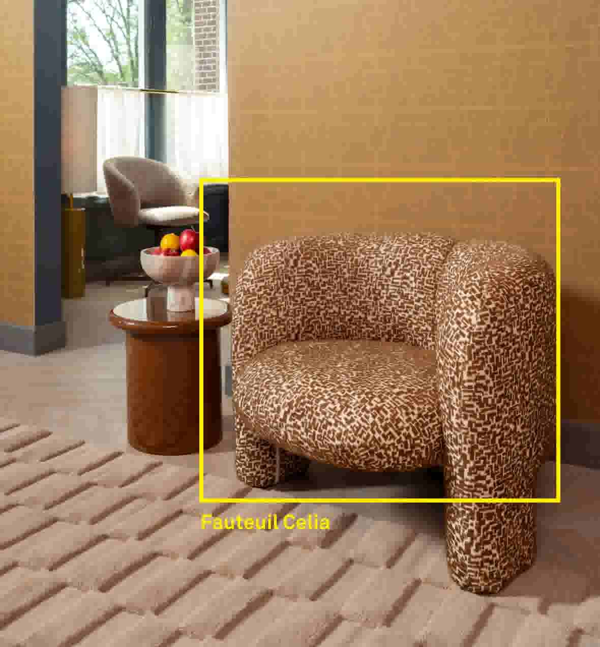 Fauteuil Celia. Product uitgelicht met gele kaderlijn: ronde fauteuil met bruin-wit grafisch patroon, in een woonkamer met bijzettafel, schaal fruit en vloerkleed.