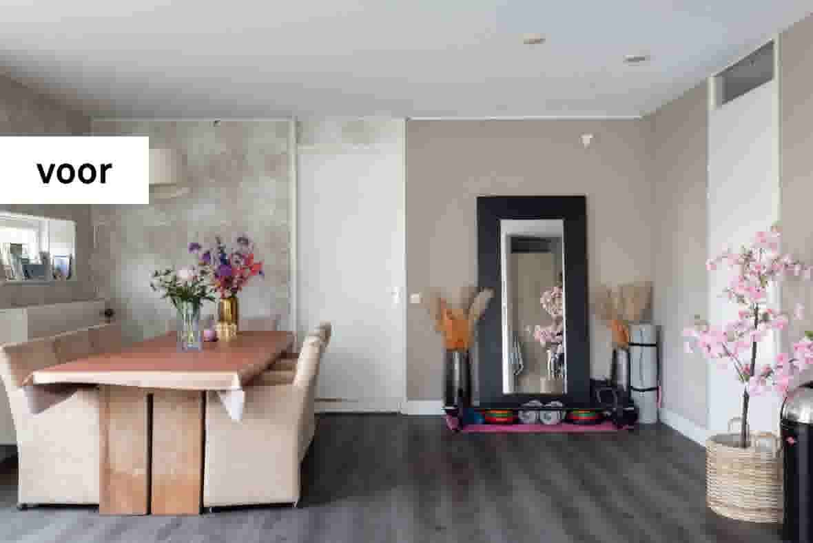 Moderne woonkamer met houten eettafel, beige bank, grote spiegel, fitnessapparatuur en roze bloesemboom decoratie.