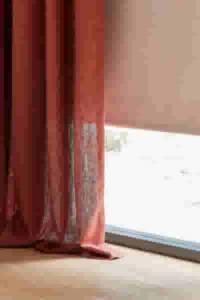 Terracotta gordijn en lichtroze rolgordijn bij een raam, met natuurlijk licht dat door de stof schijnt op een houten vloer.