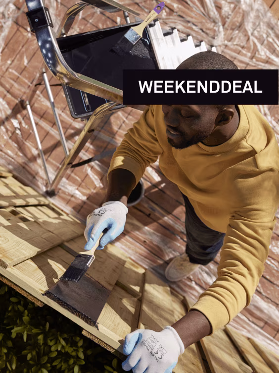 Man in gele hoodie schildert hout met zwarte verf, tekst 'WEEKENDDEAL' zichtbaar bovenaan de afbeelding.