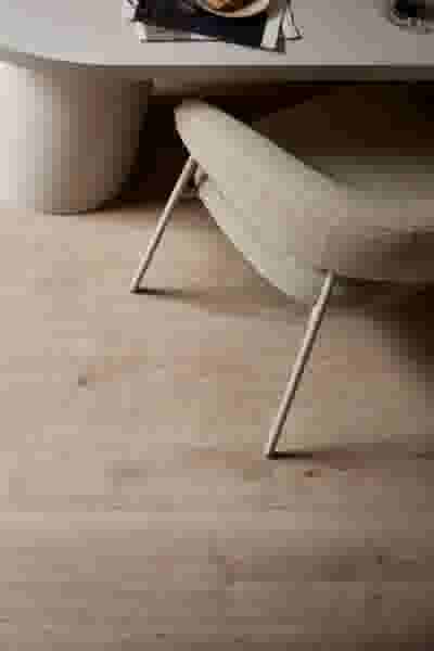 Beige stoffen stoel met metalen poten op lichte houten vloer, naast een witte pot en tafel met servies.