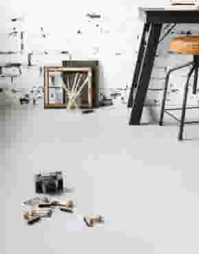 Camera met stempels, een lege schilderijlijst en een tafel met kruk op een gegoten vloer 