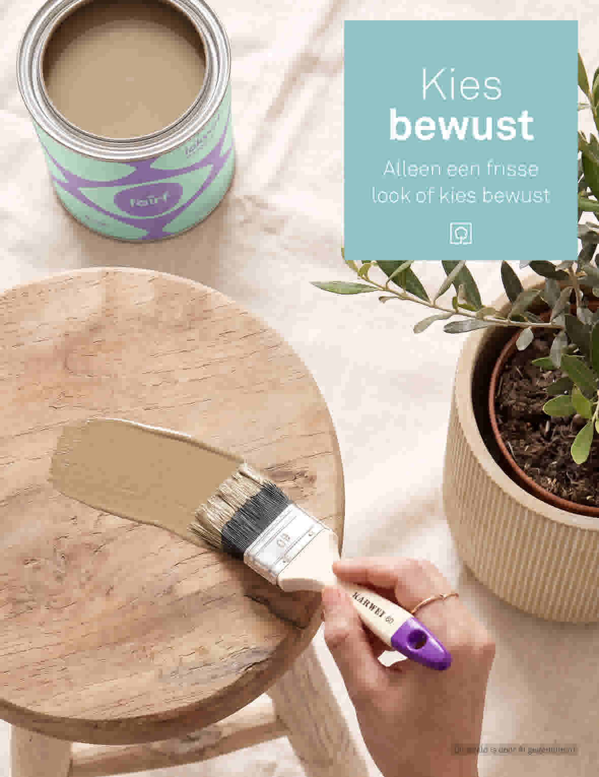 Hand met kwast schildert houten kruk met beige verf, verfblik en plant op achtergrond met turquoise kaart.