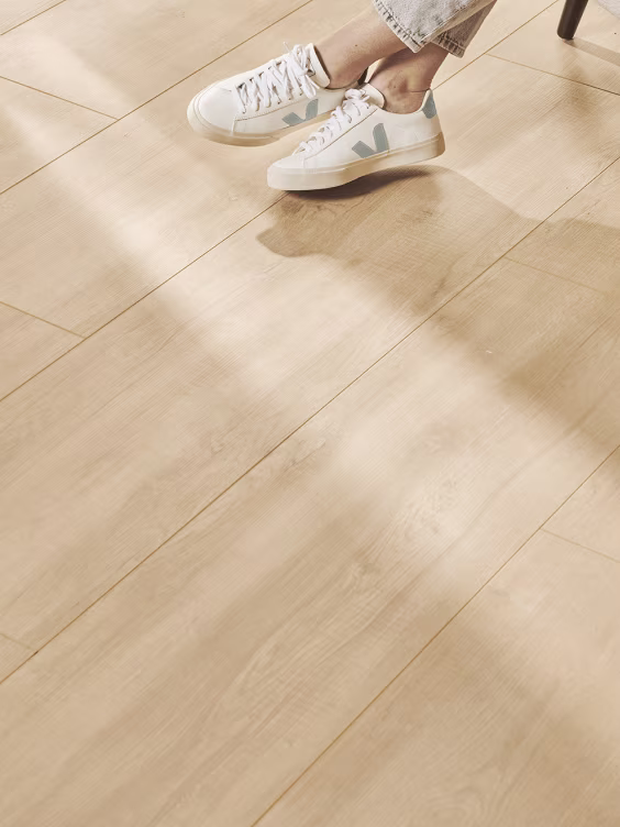 Persoon bindt witte sneakers met grijze details op lichte houten vloer met zonlicht