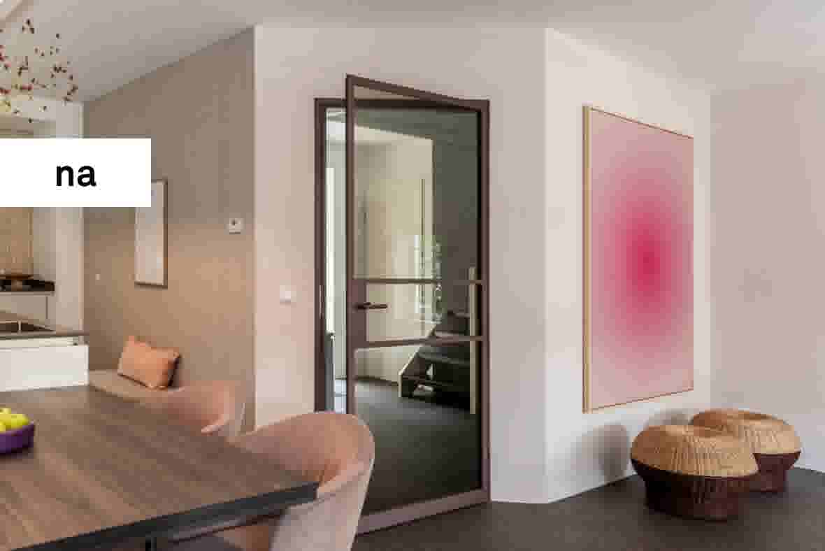 Modern interieur met glazen deur, roze stoelen aan houten tafel, roze kunstwerk en rieten poefs op grijze vloer.