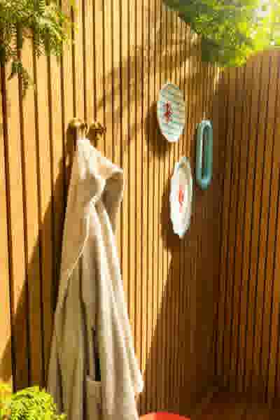 Houten wand met een beige badjas aan gouden haken en drie decoratieve borden met maritieme motieven, omgeven door groen.