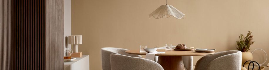 Minimalistische eetkamer met ronde houten tafel, beige stoelen, witte hanglamp en warme neutrale tinten.